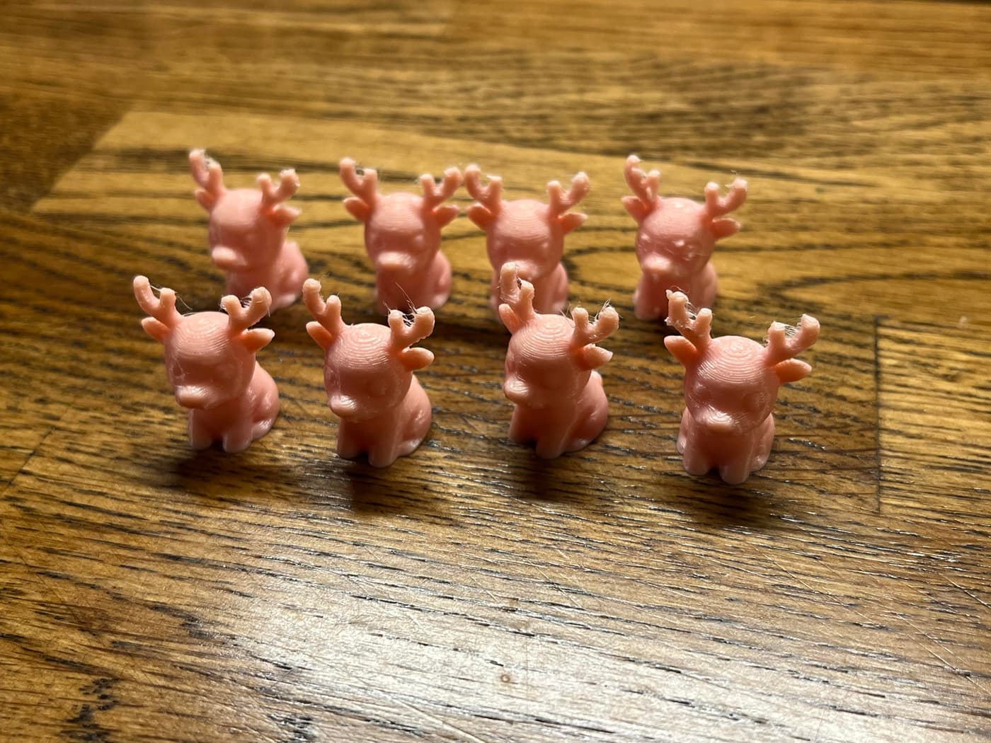A group of eight small pink plastic deer figurines with antlers, arranged in two rows on a wooden surface.