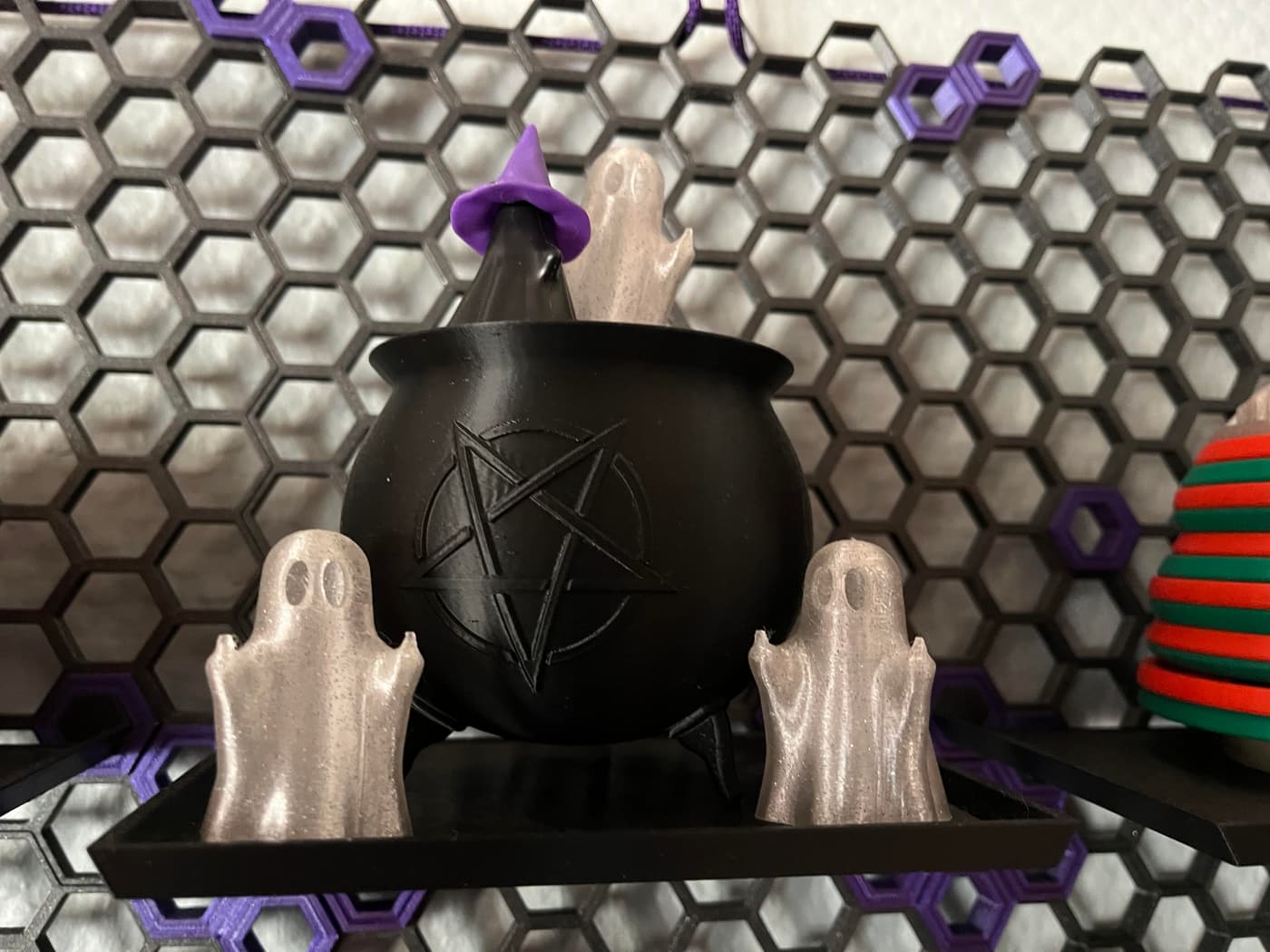 Photo of some 3D printed thingies. A few ghosts flipping the bird in semi-transparent filament around a black cauldron. There's also a black ghost with a purple witch hat