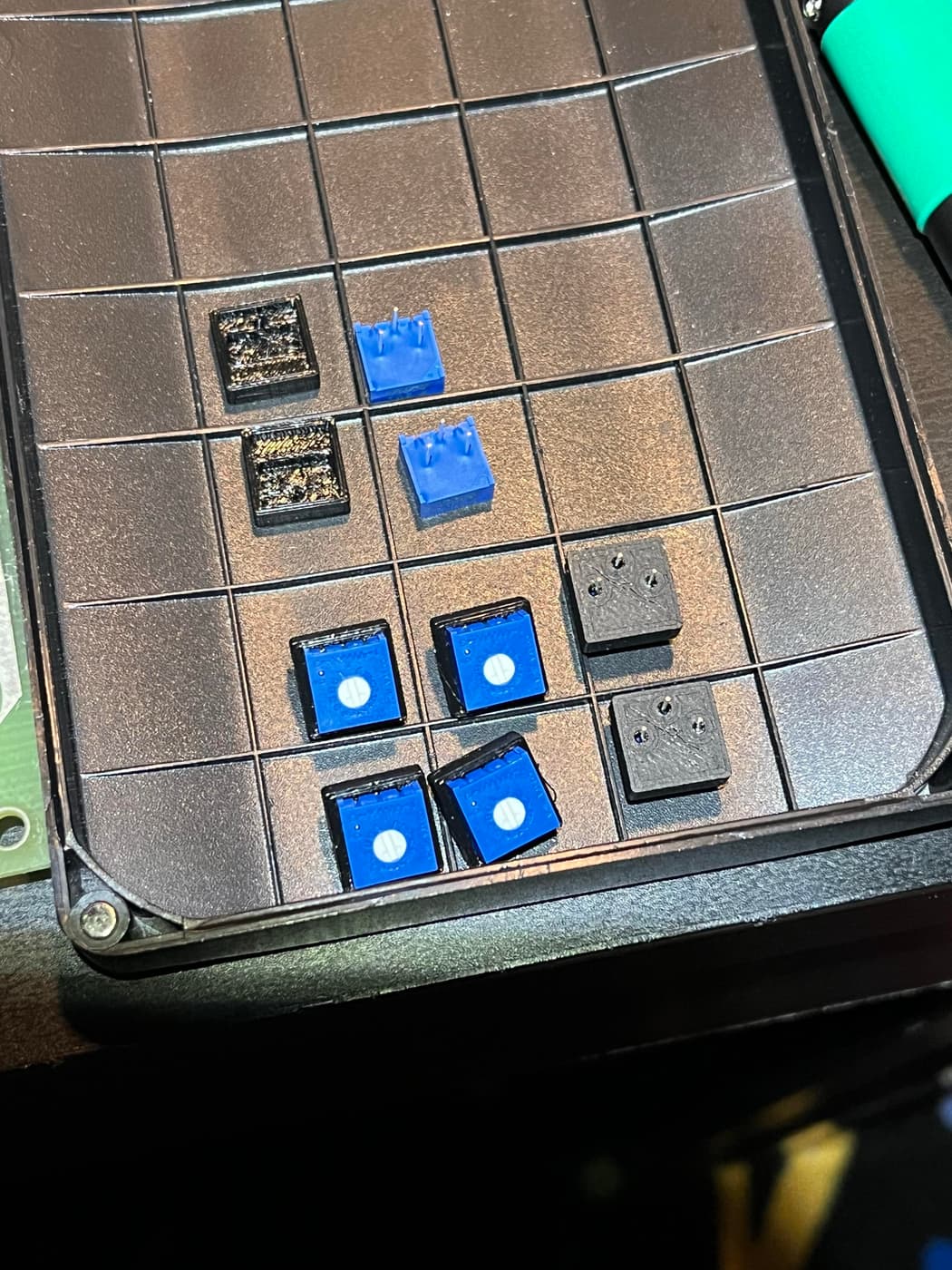 Blue potentiometers and black plastic housings laid out on a textured surface with a circuit board